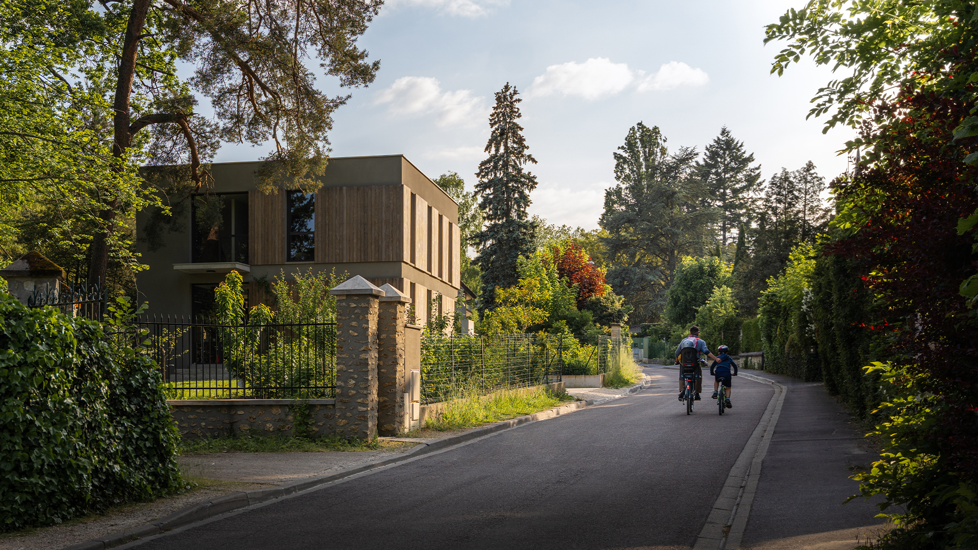 sustainable house on street with lots of trees and father and son on bikes